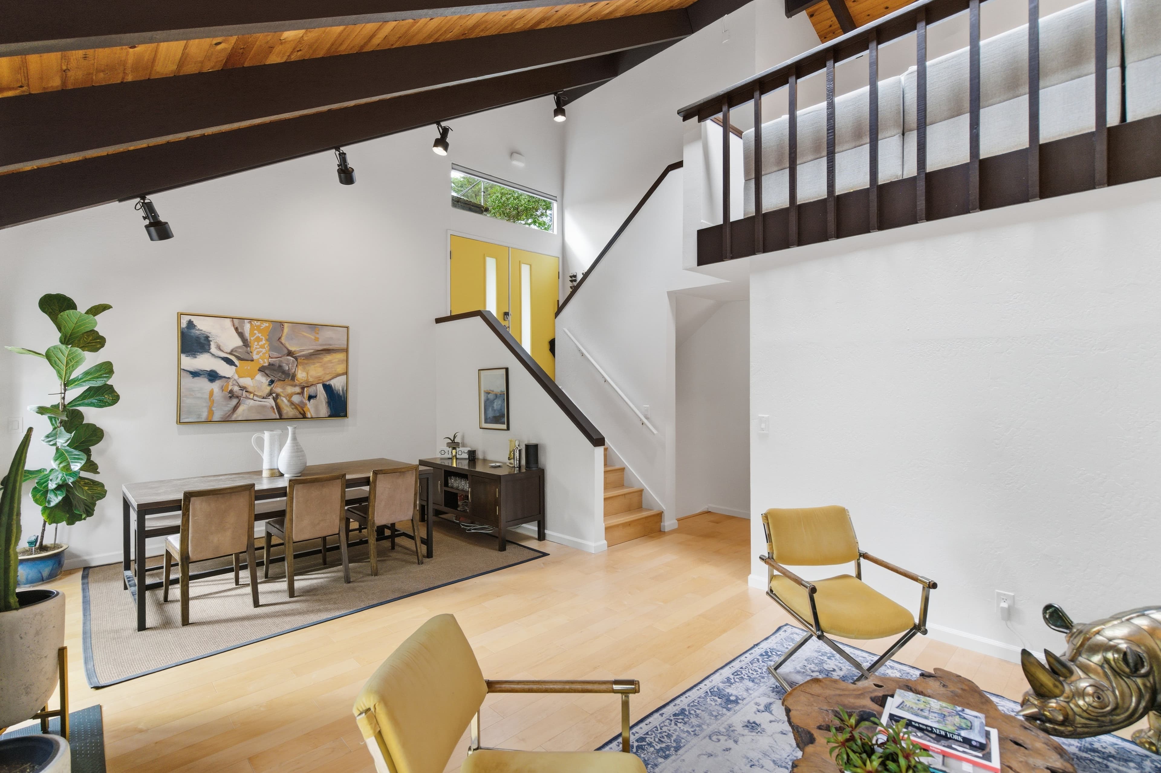 Open-concept living room with a vaulted wood ceiling, staircase, and yellow front door